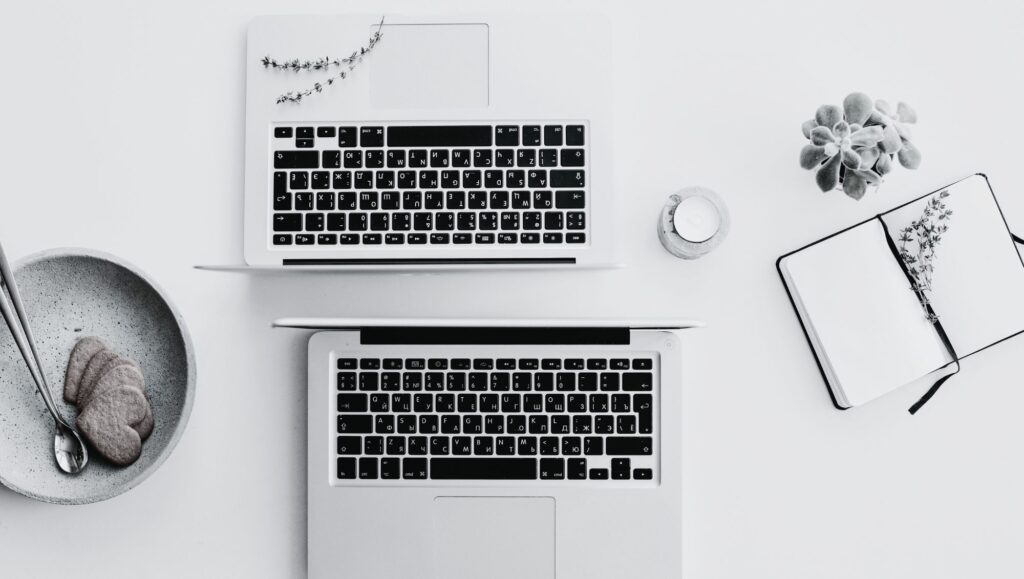 Image of minimalist desk with 2 laptops, a bowl of cookies and a notebook.