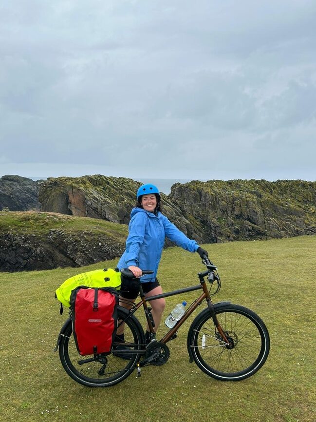 Woman stands with a bicycle against a green landscape.