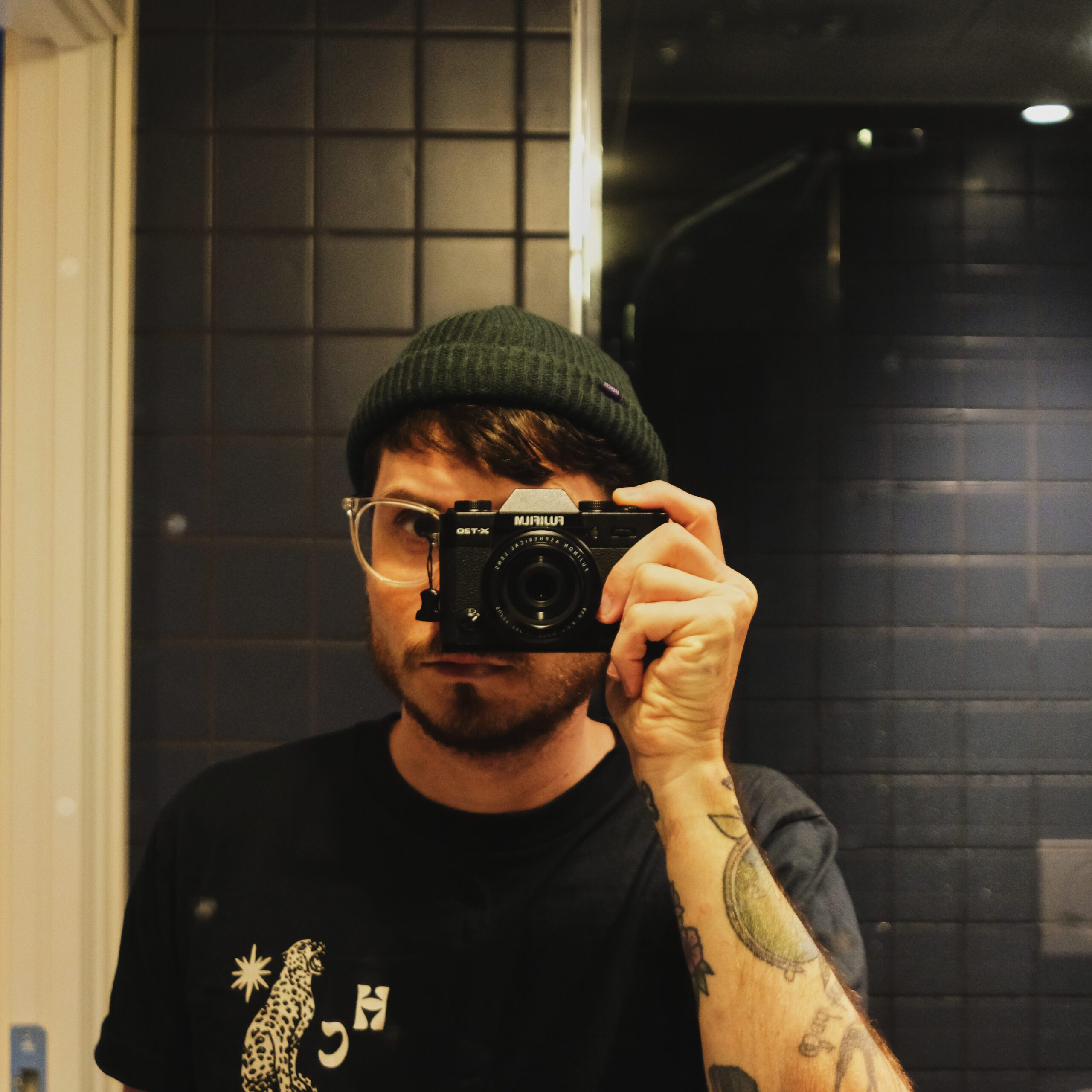 Colour image of man taking image of himself in mirror with Fujifilm camera.