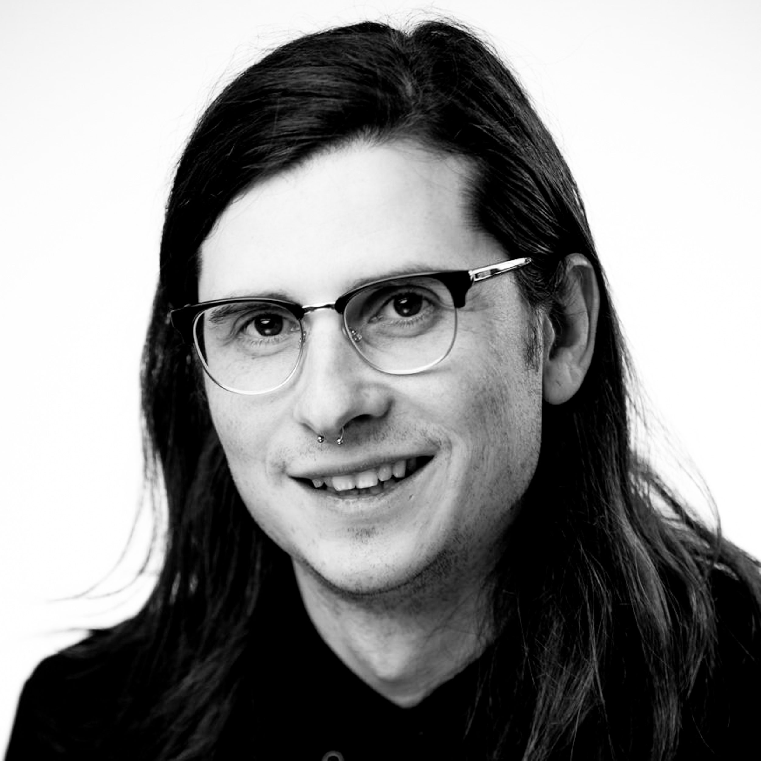Black and white image of man with long hair and glasses looking at camera.